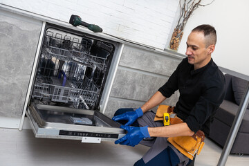 A plumber repairs a dishwasher in a kitchen room. Plumbing services. 