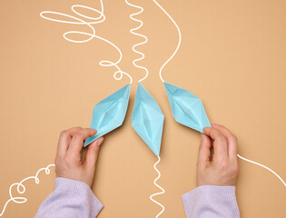 Three paper boats with different trajectories in a woman’s hand on a brown background