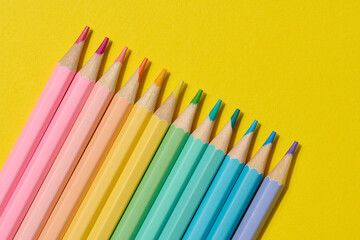 Multi-colored wooden pencils on a yellow background, top view