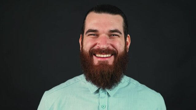 Footage of smiling bearded hipster man in casual looking at camera over dark background.