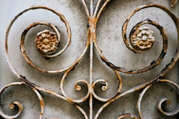 Altes verwittertes rostige Metallgitter mit Ornamentenmuster vor weißgrauer Holzfassade 