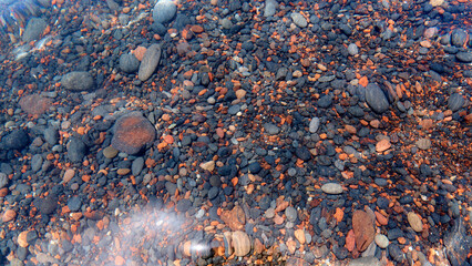 Detail of cobblestones in the transparent water of the famous Red Beach, Santorini. Background, natural stone, texture.