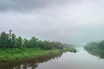 A landscape view of a calm river with green trees and mountain in India