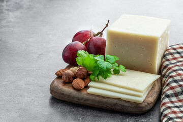 Pieces of cheese and grape on wooden board on gray background