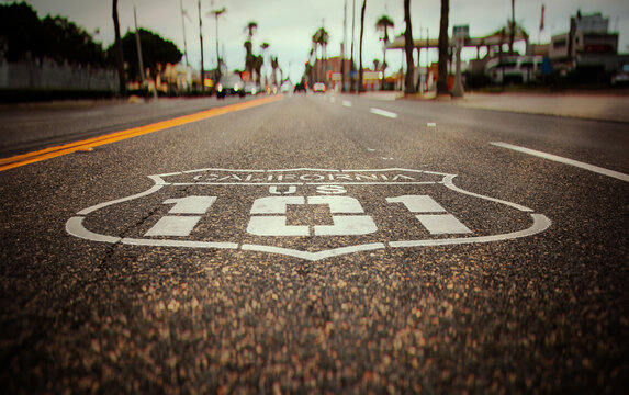 Highway 101 sign painted on the black asphalt road with city diffused in the background. The shot has vintage tones and is from Oceanside California
