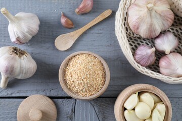 Dehydrated garlic granules and fresh bulbs on grey wooden table, flat lay