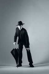 a full-length portrait of a young man in a suit with a hat and an umbrella, shot in a studio in black and white