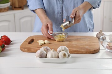 Woman squeezing garlic with press at white wooden table in kitchen, closeup - obrazy, fototapety, plakaty