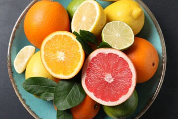 Different cut and whole citrus fruits on black table, top view