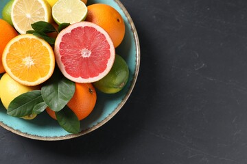 Different cut and whole citrus fruits on black table, top view. Space for text