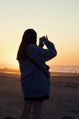 Fototapeta premium Mujer tomando una fotografía con su teléfono móvil en la playa durante el atardecer