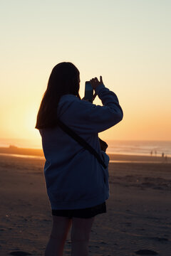 Mujer tomando una fotografía con su teléfono móvil en la playa durante el atardecer