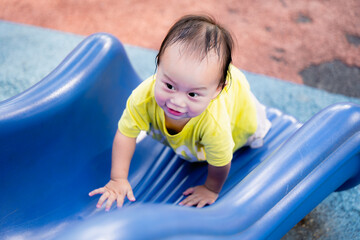 Fototapeta na wymiar Portrait of Asian Baby Boy happily playing on the playground, and sliding down a blue slide. Cute kid climbs the slide on the playground. Toddler child aged one-year-old. Real People.