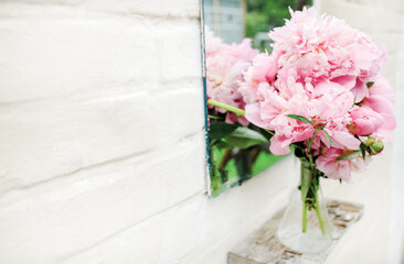Bouquet of peonies near mirror outdoors near white brick wall