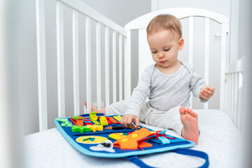 Baby playing with montessori busy book sitting in crib. Concept of smart books and modern toys