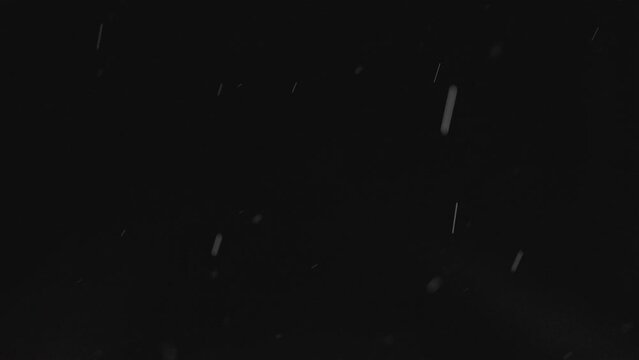 Slow motion raindrops falling from the right at night on a dark black background