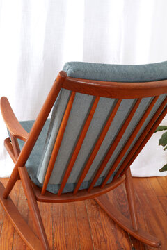 Mid-Century Modern Rocking Chair. Vintage Teak Furniture. 1950s Design. Interior photograph before a luxurious white curtain with houseplants. Close-up detail.