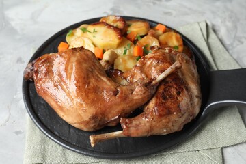 Tasty cooked rabbit meat with vegetables on light grey table, closeup