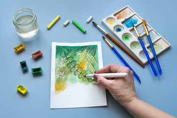 watercolor paintings of green leaves and flowers  with paintbrushes and watercolor paints. Artist's...