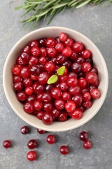 Fresh ripe cranberries in bowl and rosemary on grey table, flat lay