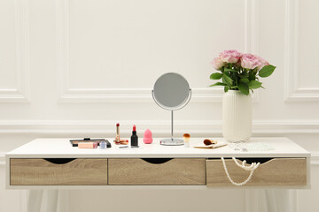 Mirror, cosmetic products, jewelry and vase with pink roses on white dressing table in makeup room