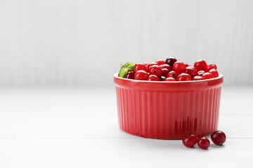 Fresh ripe cranberries in bowl on white wooden table, closeup. Space for text