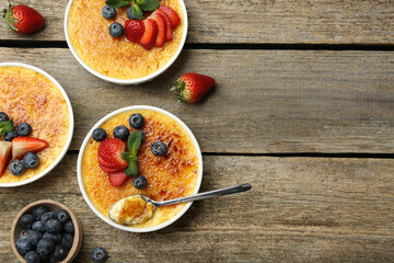 Flat lay composition with delicious creme brulee with berries and mint in bowls on wooden table....