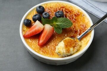 Delicious creme brulee with berries in bowl and spoon on grey table, closeup