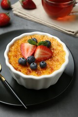 Delicious creme brulee with berries and mint in bowl on grey table, closeup