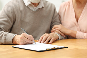 Senior couple signing Last Will and Testament at wooden table, closeup