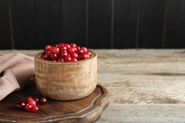 Cranberries in bowl on wooden table, space for text