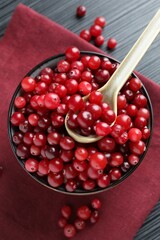 Cranberries in bowl and spoon on black wooden table, top view