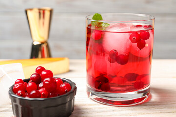 Tasty cranberry cocktail with ice cubes in glass and fresh berries on wooden table