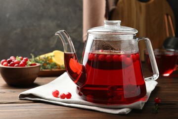 Tasty hot cranberry tea in teapot and fresh berries on wooden table