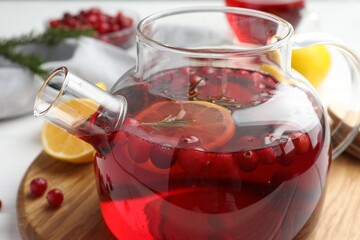Tasty hot cranberry tea with lemon, rosemary and fresh berries in teapot on table, closeup