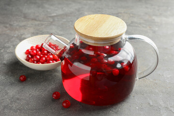 Tasty hot cranberry tea in teapot and fresh berries on light grey textured table