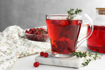 Tasty hot cranberry tea with thyme and fresh berries in glass cup on white wooden table