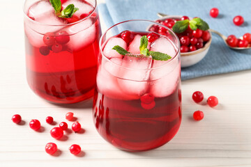 Tasty cranberry juice with ice cubes in glasses and fresh berries on white wooden table, closeup