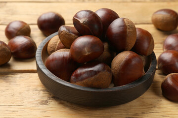 Sweet fresh edible chestnuts in bowl on wooden table, closeup