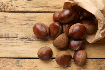 Sweet fresh edible chestnuts in paper bag on wooden table, top view. Space for text