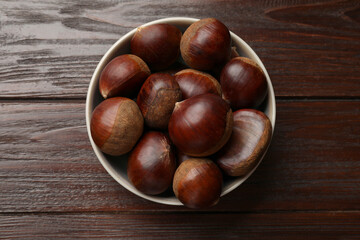 Sweet fresh edible chestnuts in bowl on wooden table, top view