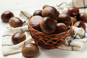 Sweet fresh edible chestnuts in wicker bowl on white table, closeup