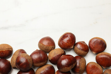 Sweet fresh edible chestnuts on white marble table, top view. Space for text