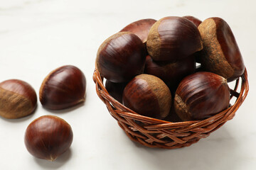 Sweet fresh edible chestnuts in wicker bowl on white table, closeup