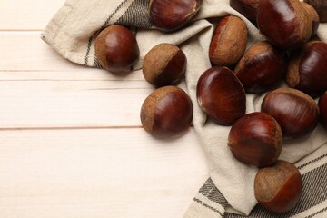 Sweet fresh edible chestnuts on light wooden table, top view. Space for text