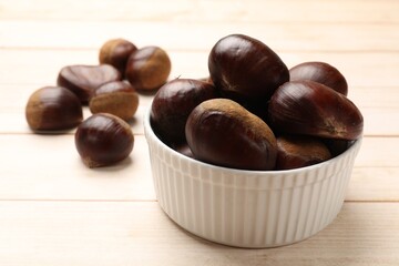 Sweet fresh edible chestnuts on light wooden table, closeup