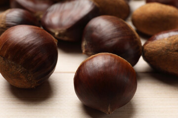 Sweet fresh edible chestnuts on light wooden table, closeup