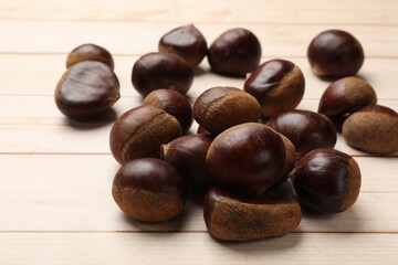 Sweet fresh edible chestnuts on light wooden table, closeup