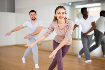 Portrait of cheerful young woman enjoying active dancing during group training in dance studio..