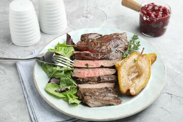 Delicious roasted beef meat, caramelized pear and greens served on light textured table